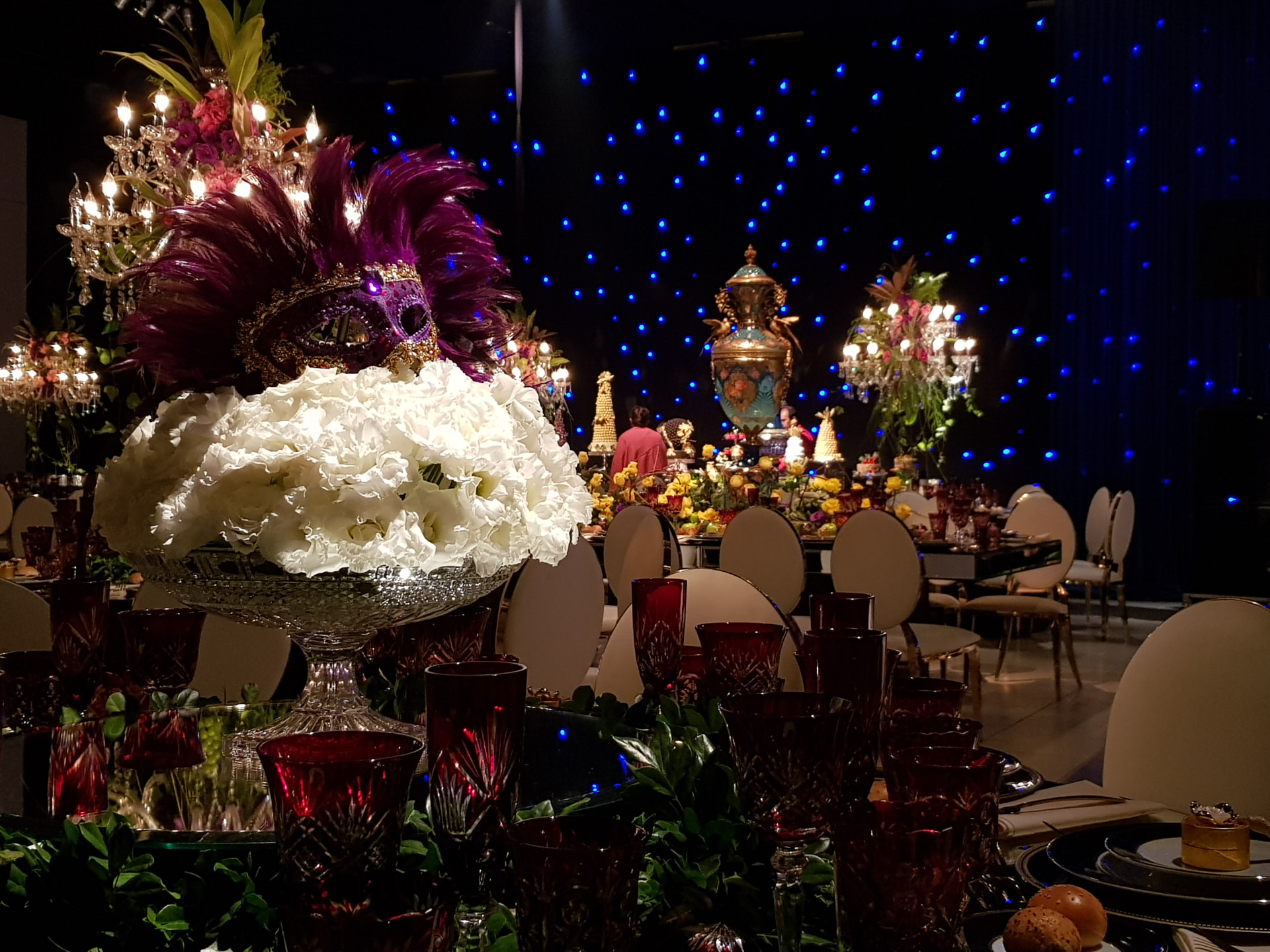 Mesa de gala con máscara veneciana, cristalería roja y telón de estrellas